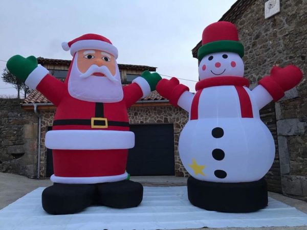 Structures gonflables dans le thème de Noël, un bonhomme de neige géant et un père noel géant devant une maison en pierre, Jump'O'Clown