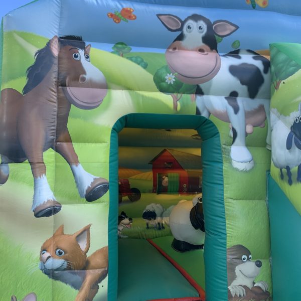 Zoom sur la Structure gonflable, château gonflable, maison toboggan ferme avec obstacle mouton noir et blanc vert avec un fond de dessins d'animaux de la ferme, dans un jardin, Jump'O'Clown