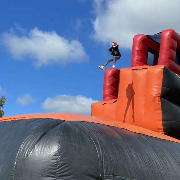 Structure gonflable vu de côté avec une personne qui saute, animation X Treme Jump, matelas gonflable géant rouge et noir, Jump'O'Clown