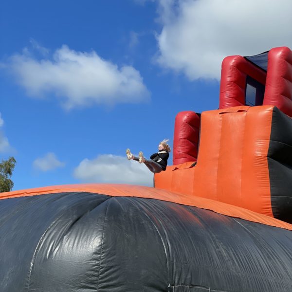 Structure gonflable vu de côté avec une personne qui saute, animation X Treme Jump, matelas gonflable géant rouge et noir, Jump'O'Clown